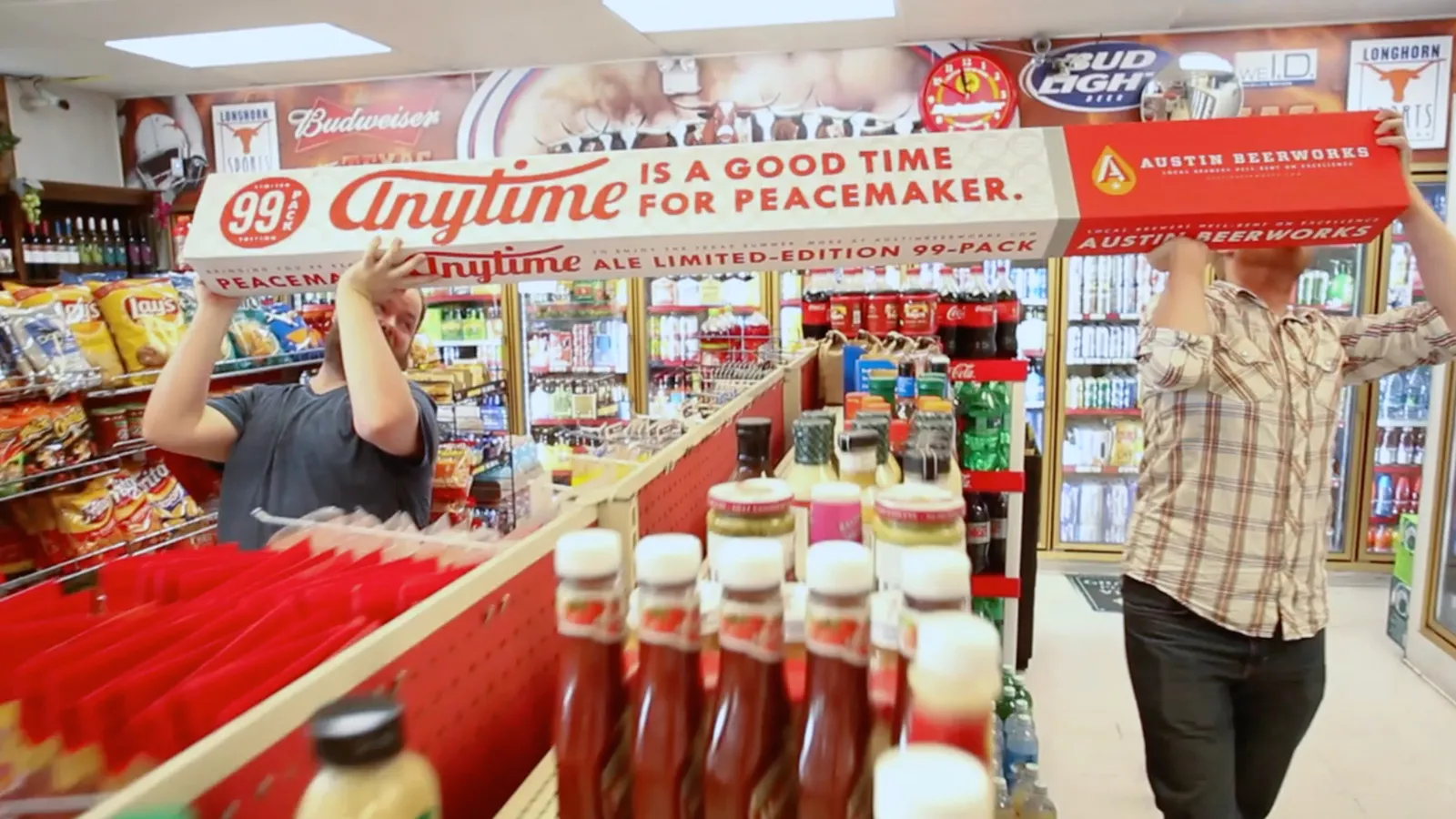 Two people at a convenience store checkout, one reaching for items, shelves with drinks and snacks visible.