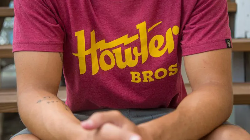 Person wearing a maroon T-shirt with yellow text reading 'Howler BROS' sitting outdoors.
