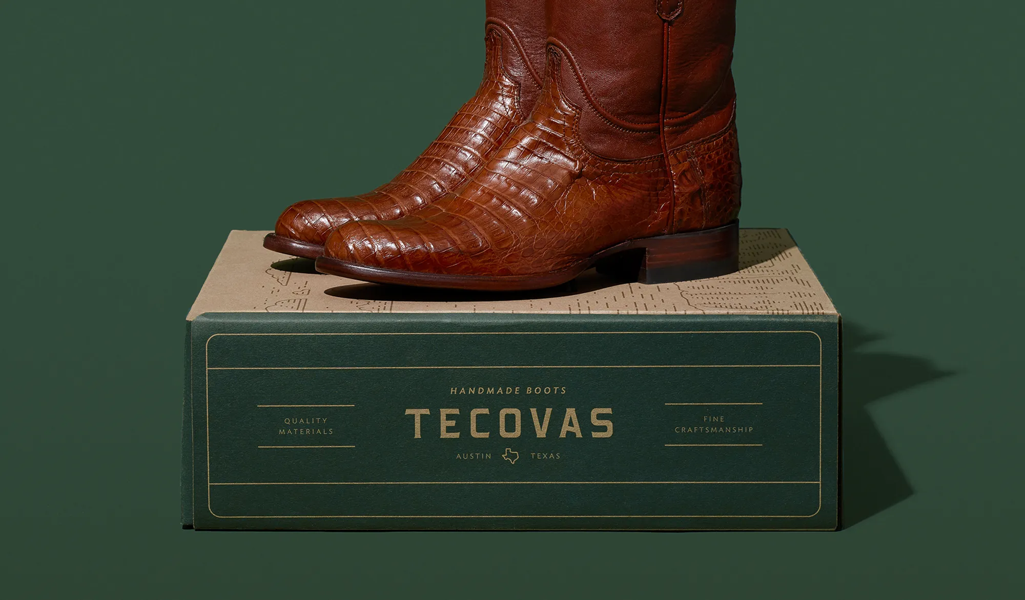 A brown cowboy boot displayed on a box with the brand name Tecovas, against a green background.