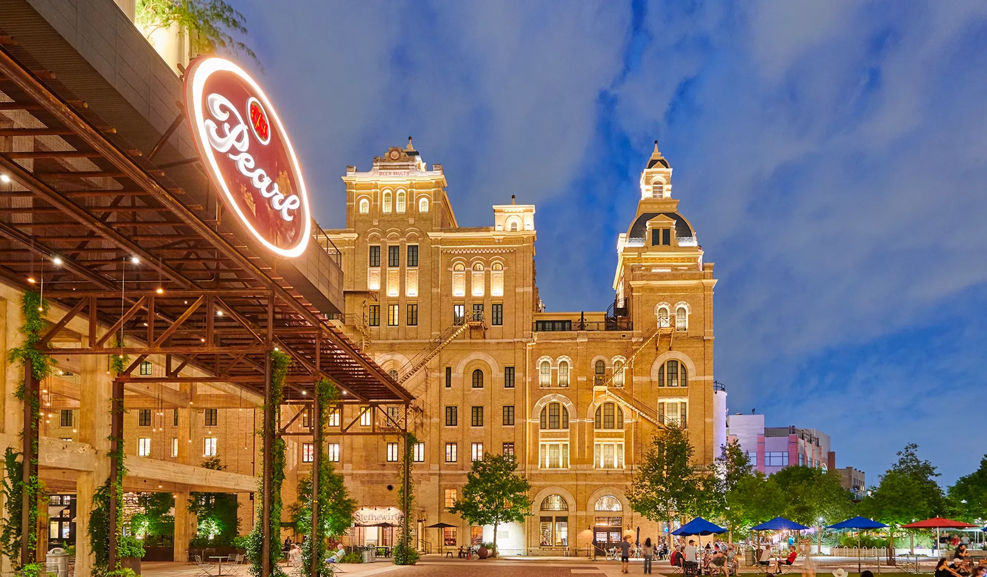 Historic building with towers and a neon sign reading 'Brewery' against a blue sky with clouds.