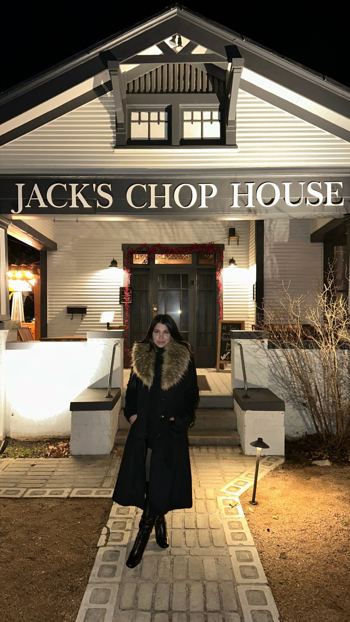 Person standing outside Jack's Chop House at night, building with sign, lit windows, and pathway.