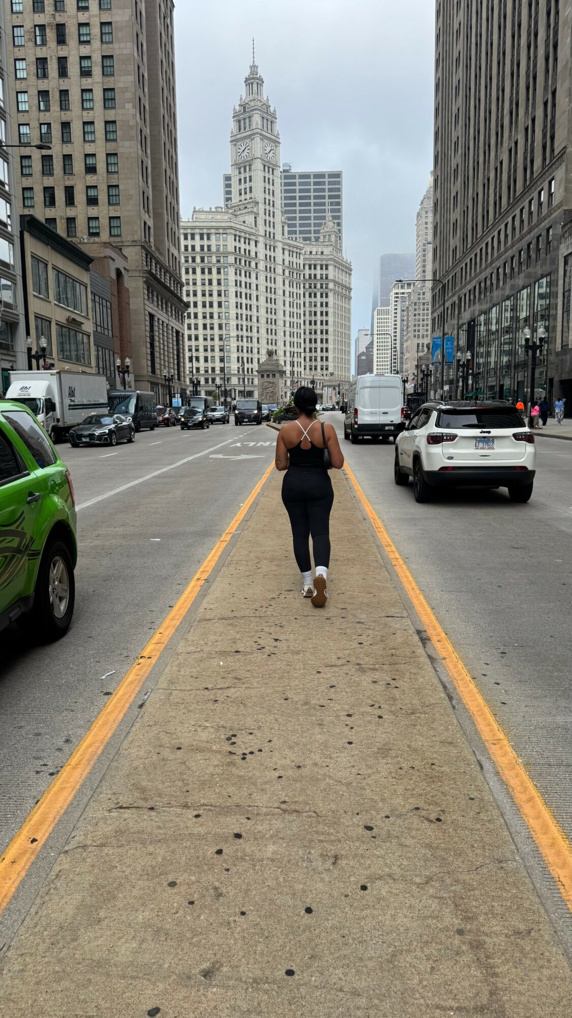 Person walking on a city street with tall buildings and a clock tower in the background.