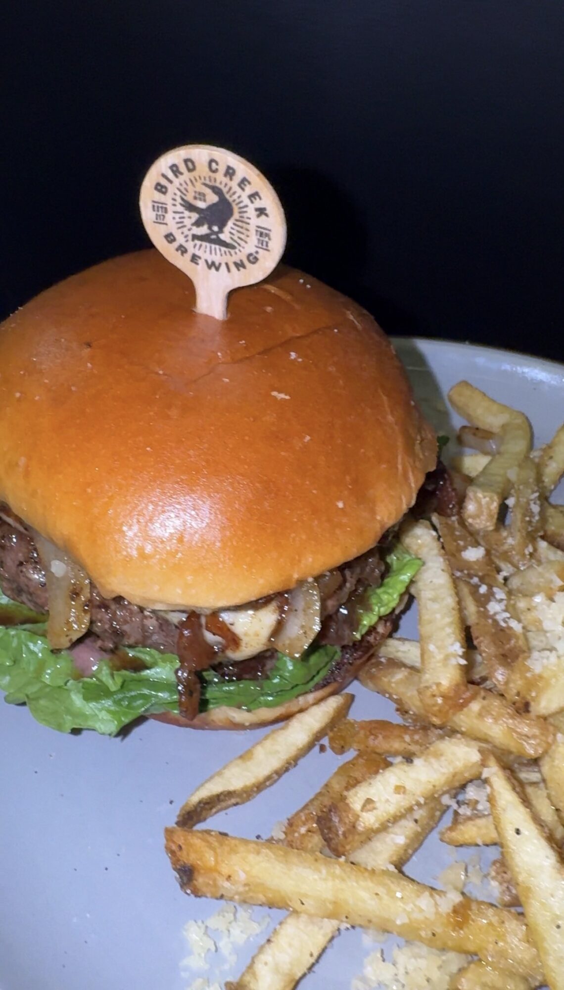 Burger with lettuce, beef patty, and bun, served with French fries on a plate.