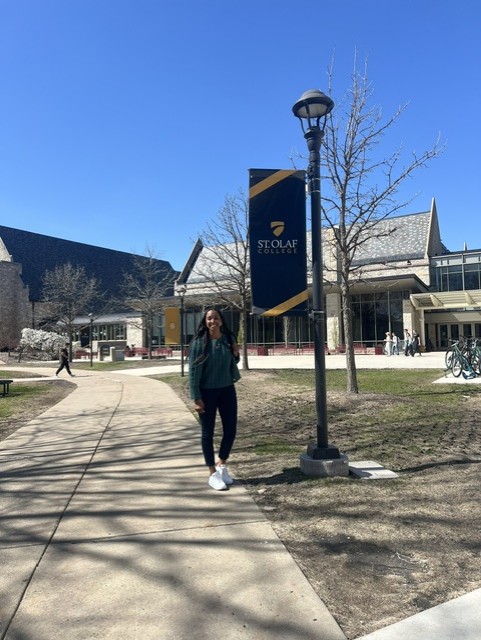 Person walking on sidewalk near lamppost with sign, buildings in background, clear blue sky.