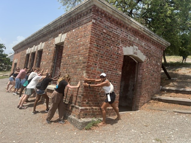 Group of people pushing against a brick building with an arched entrance, outdoors on a sunny day.