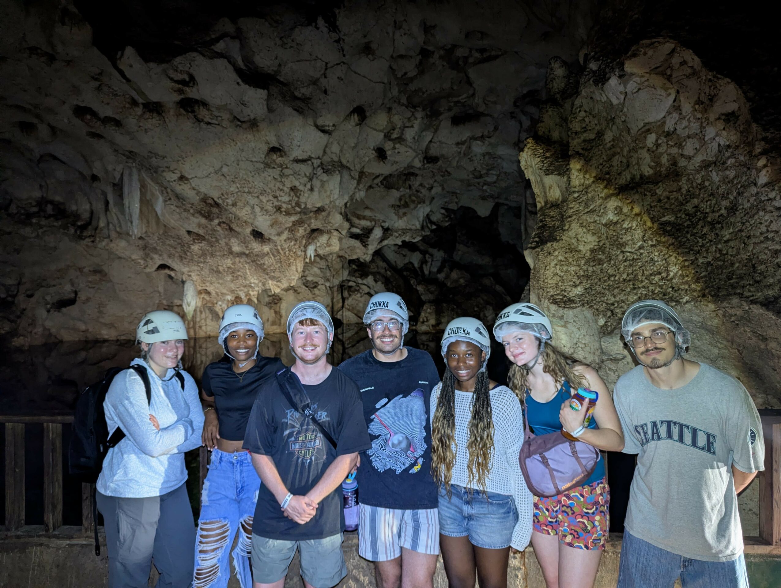 Group of seven people wearing helmets inside a cave with rocky walls.