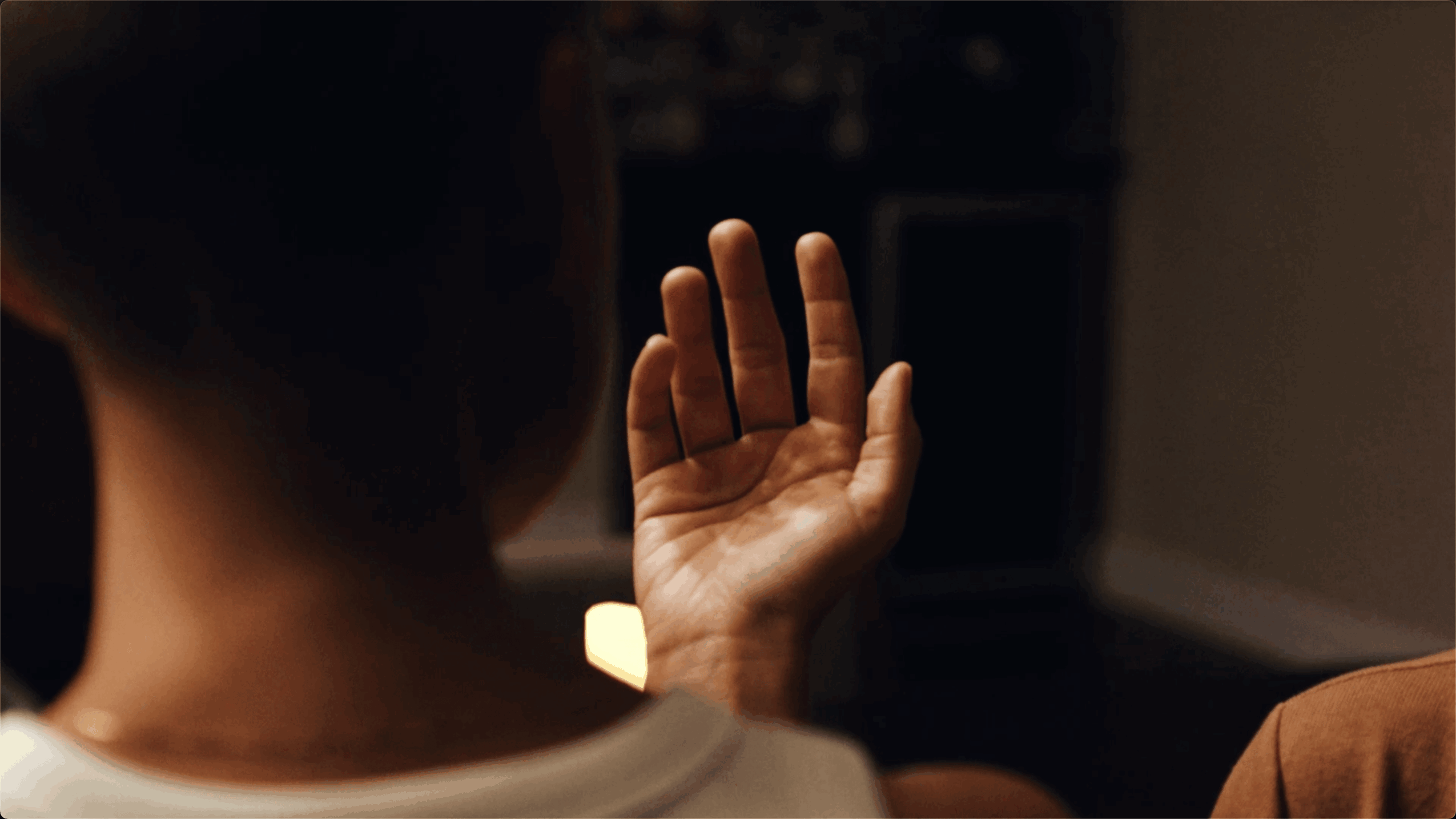Person with raised hand, viewed from behind, in a dimly lit room.