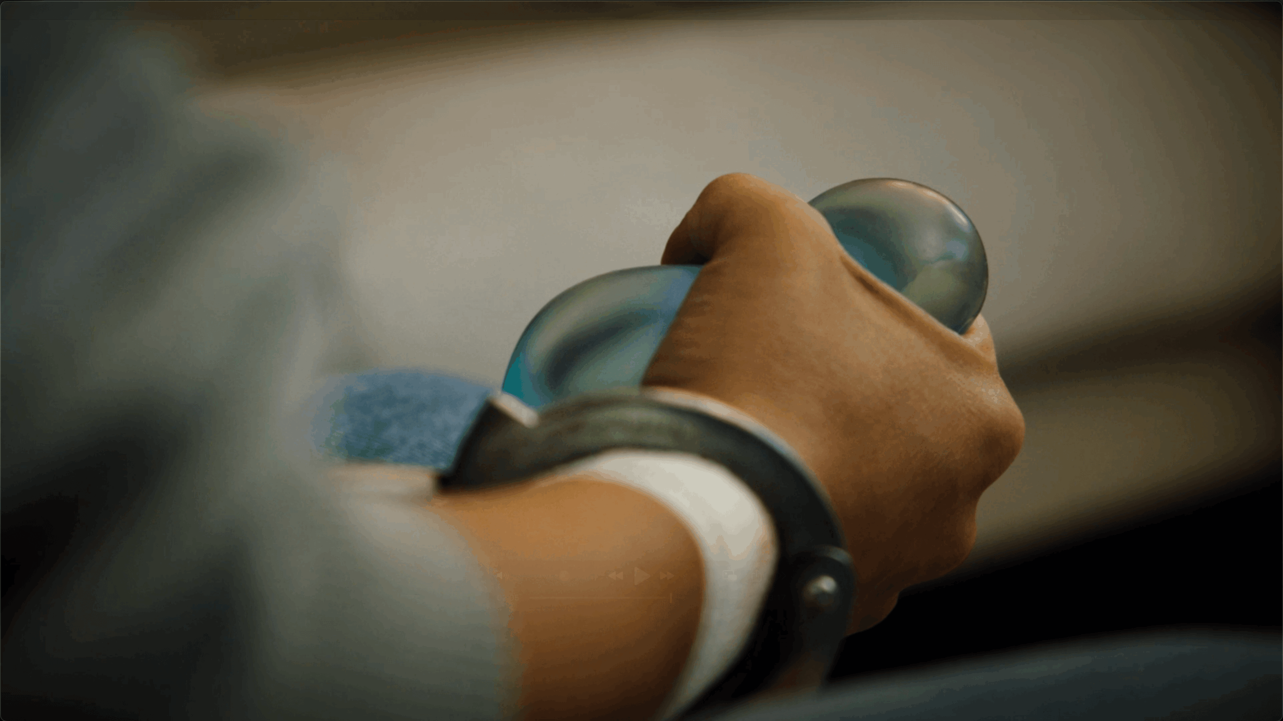 Close-up of a person's hand gripping a steering wheel, with a blurred background.