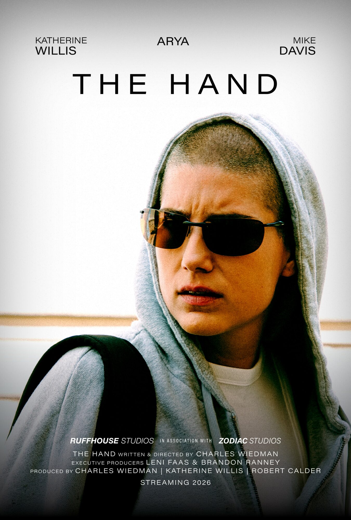 Young person wearing sunglasses and hoodie, looking serious, with a plain background.
