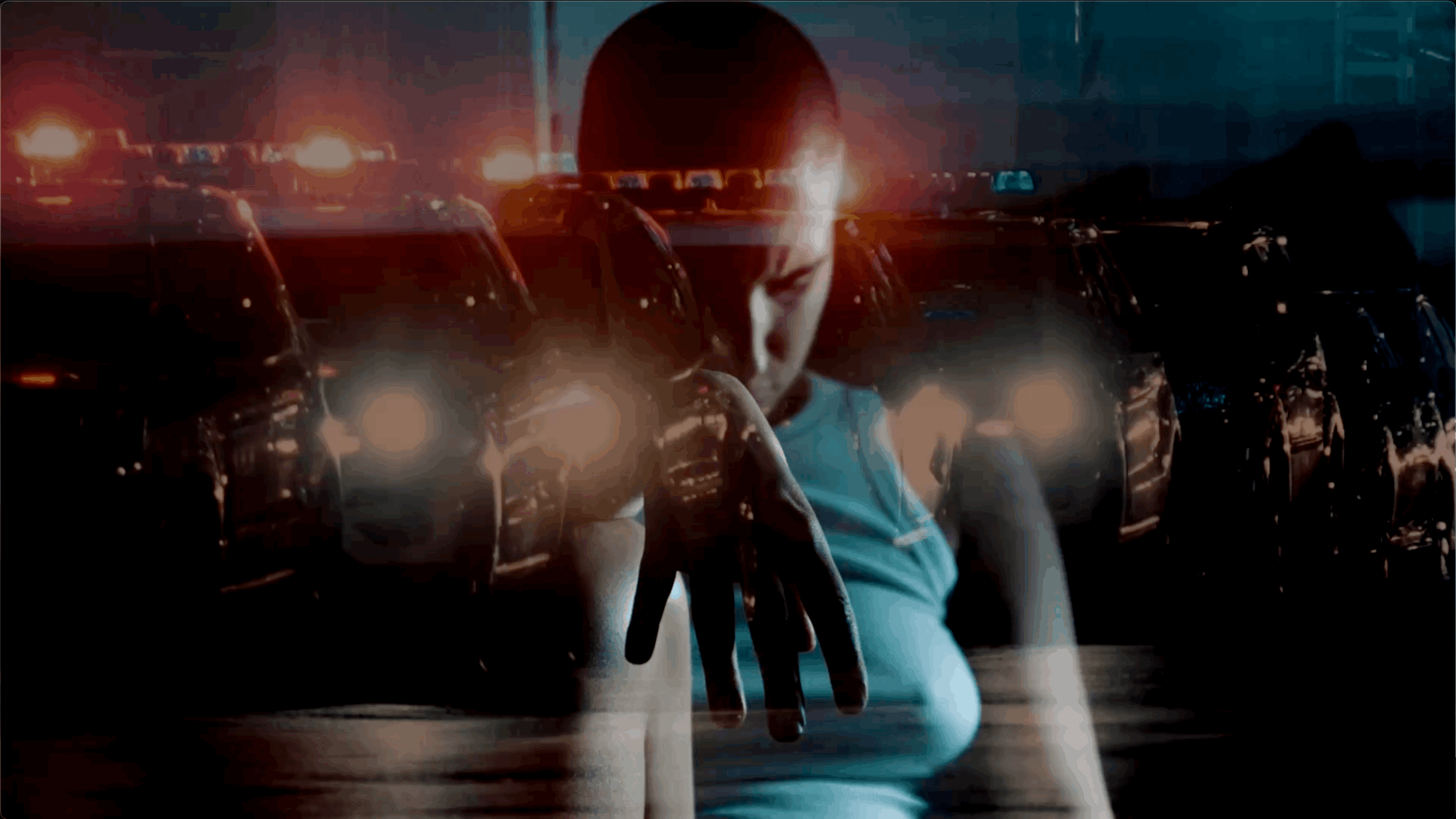 Person with hand extended forward, cars with headlights on in the background, dark and moody lighting.