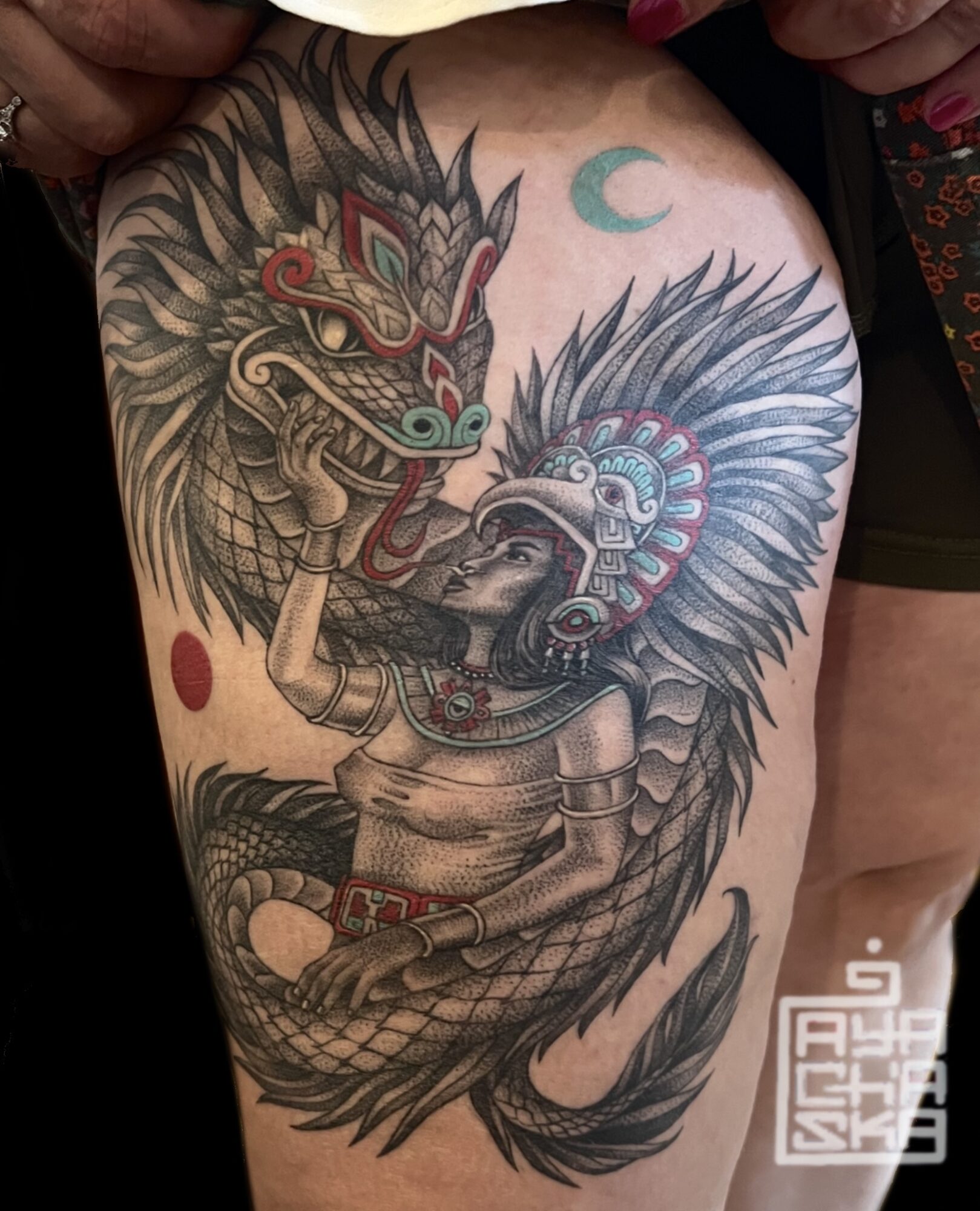 Tattoo of a lion and dragon with a crescent moon and red circle, detailed with scales and feathers, on a person's shoulder.