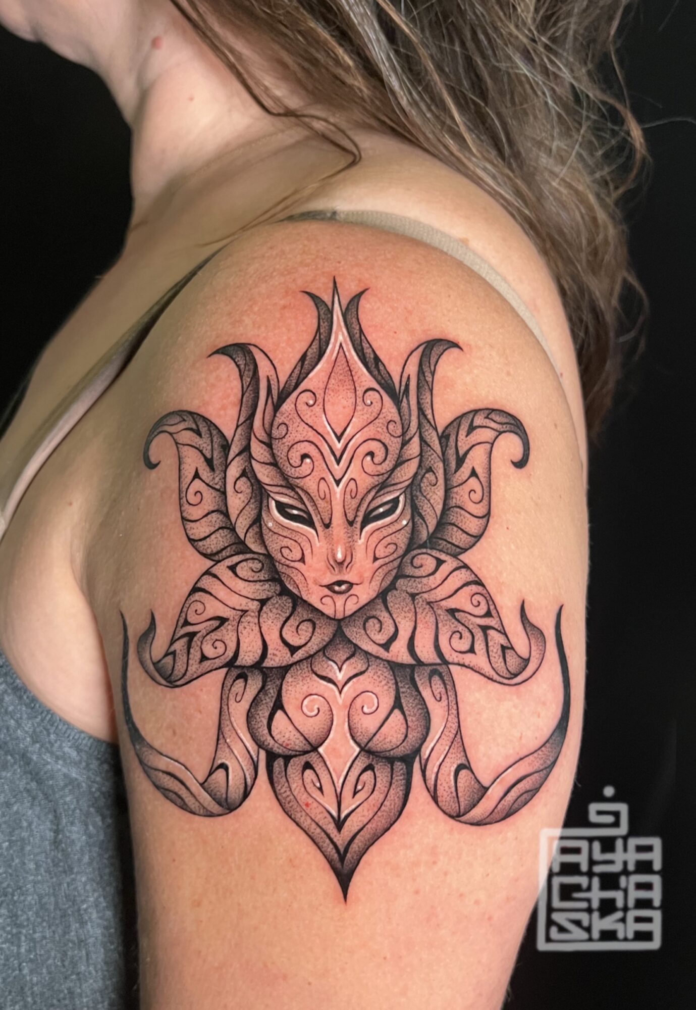 Tattoo of a stylized, symmetrical creature with intricate patterns on shoulder, featuring horns, wings, and detailed line work.