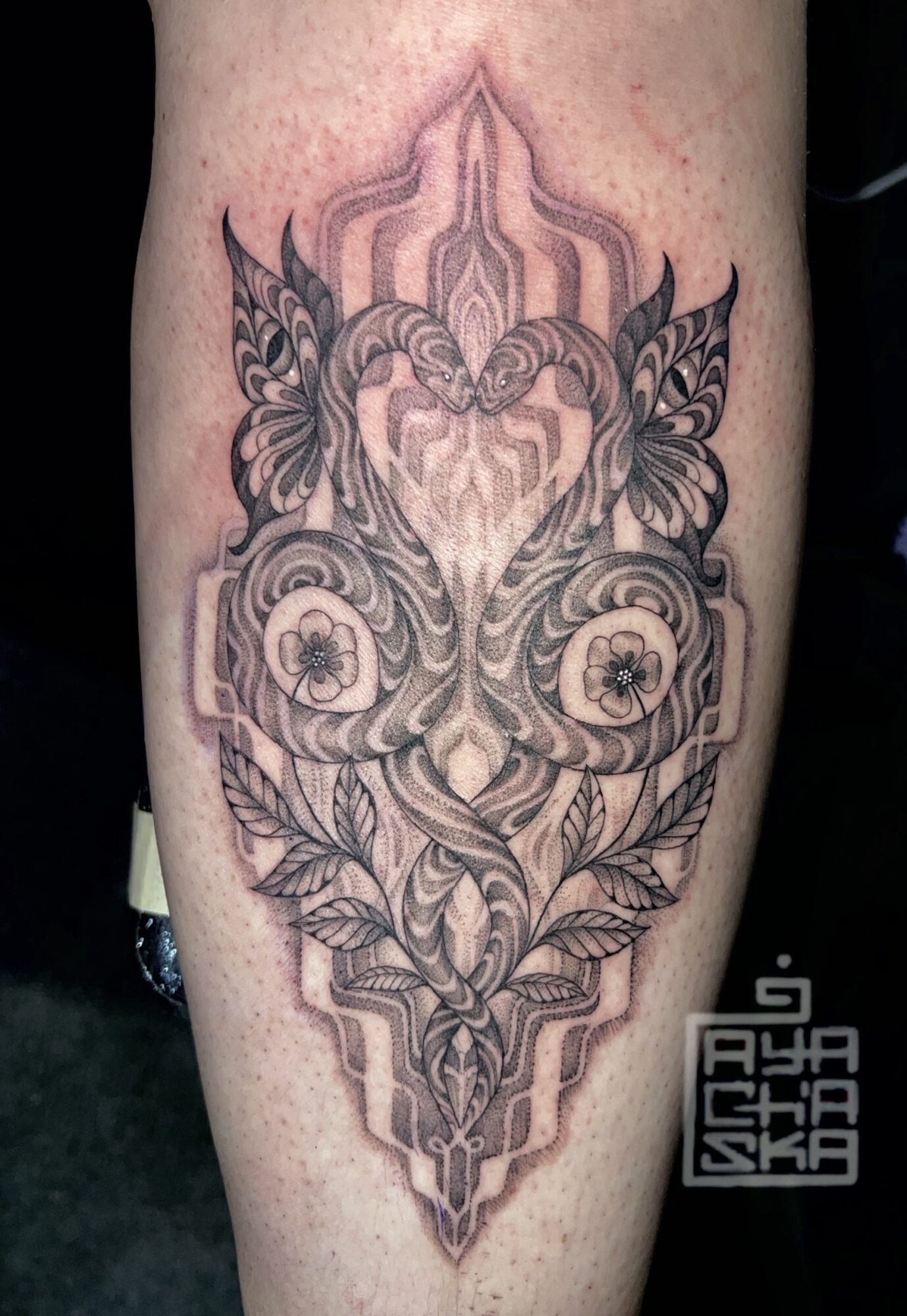 Tattoo with symmetrical geometric and floral patterns, featuring a heart shape at the center, on skin.