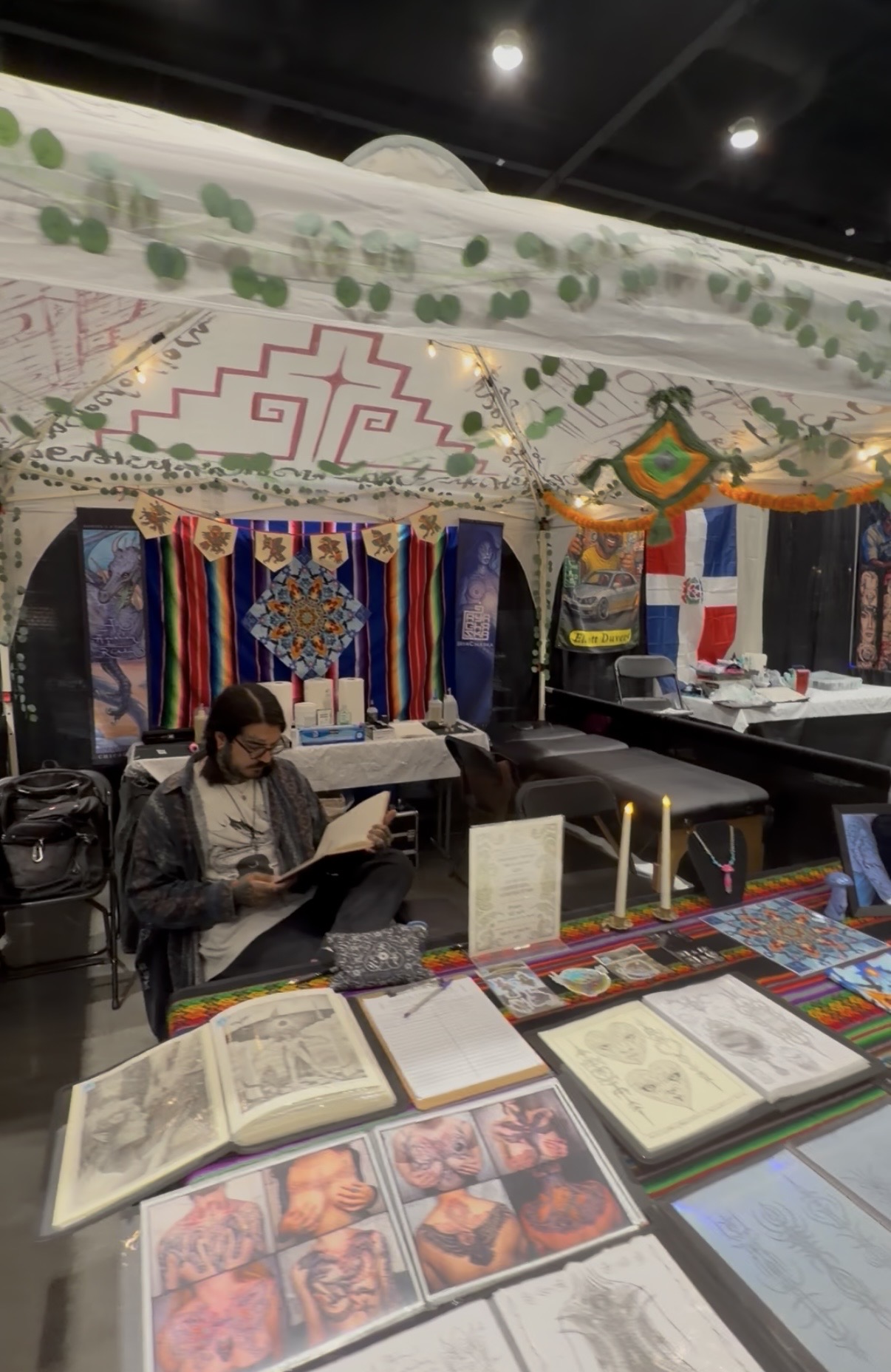 Person sitting at a table with open books, decorated with colorful textiles and traditional items in the background.