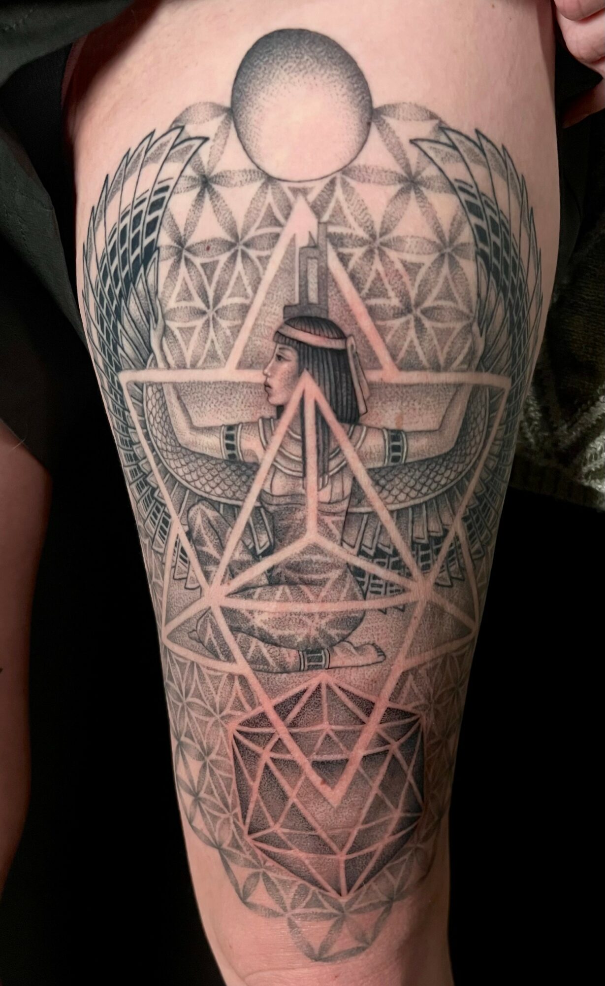 Tattoo of geometric patterns, a pyramid, and a person with wings on the thigh.