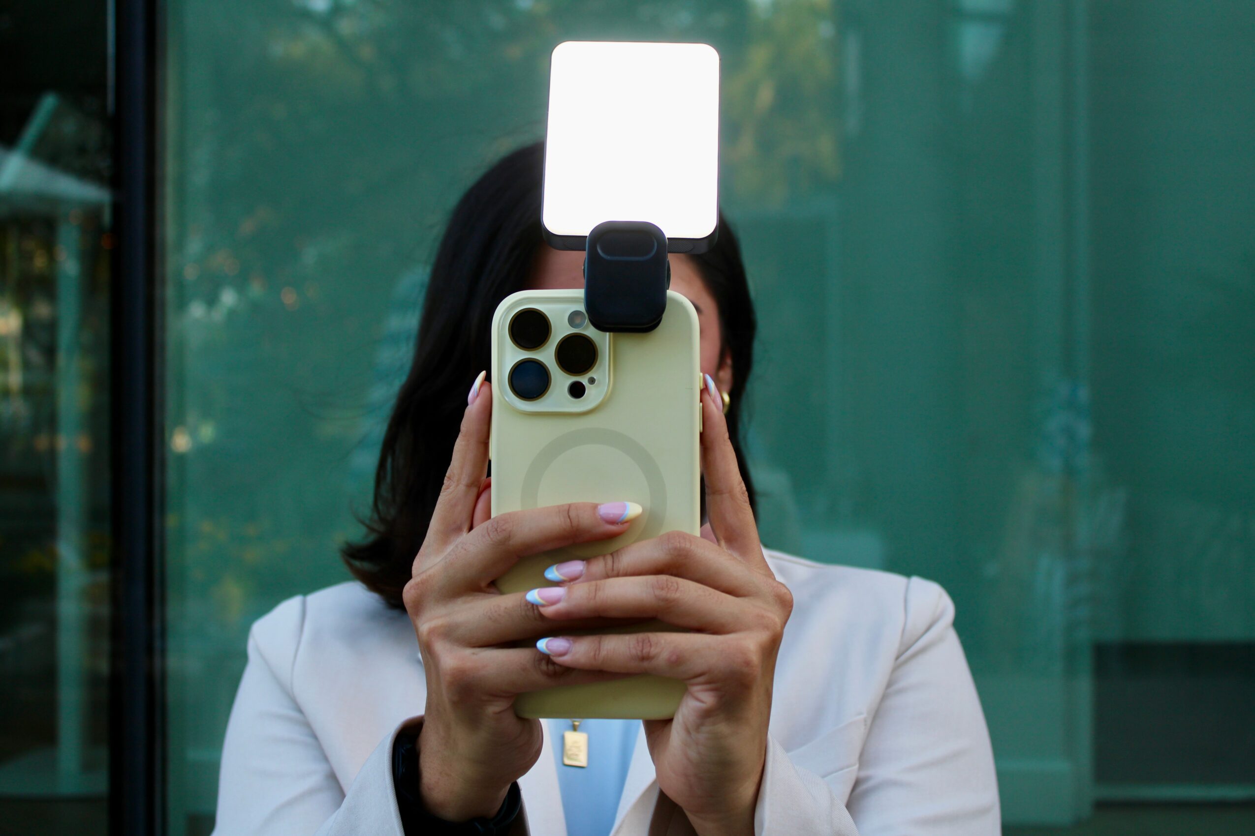 Person holding a smartphone in front of their face, with a bright light reflecting off the phone's screen, background of glass window.