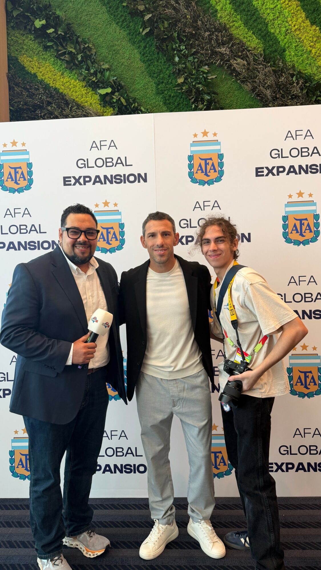 Three people standing in front of a backdrop with text and logos, smiling for the photo.