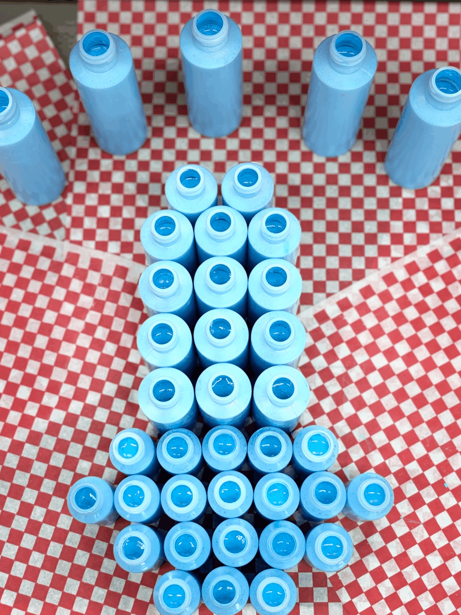 Blue bottles arranged on a red and white checkered surface, forming a shape resembling a rocket or bottle with a tail.