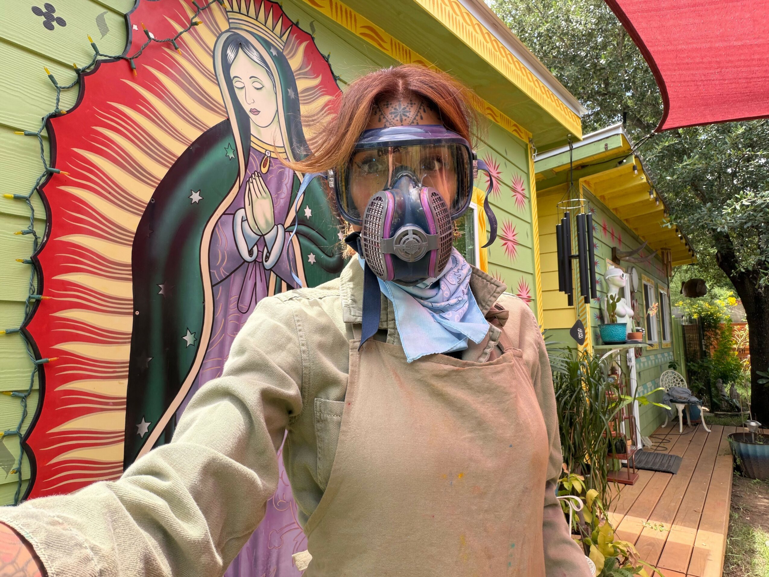 Person wearing a mask and glasses standing in front of colorful mural with a woman and sun design.