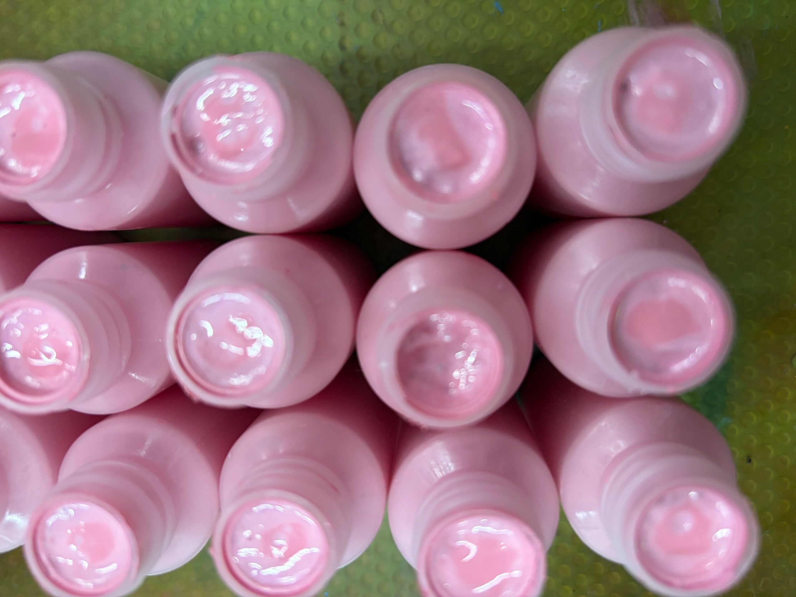 Top view of ten pink bottles arranged in two rows on a green surface, showing the bottle caps and openings.