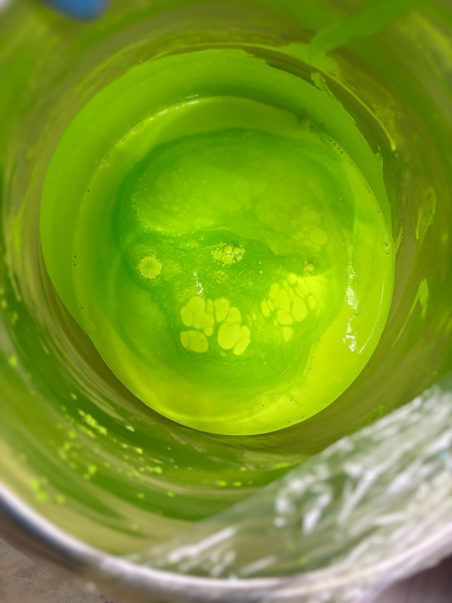 Green liquid inside a container with bubbles and foam, viewed from above.