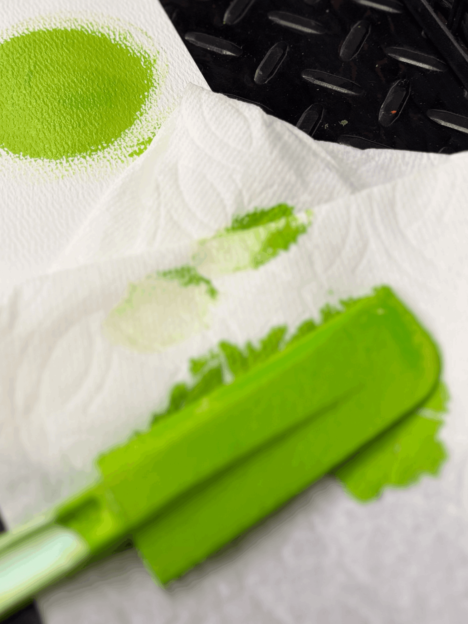 Celery stalk and a small pile of green powder on a paper towel, with a black textured surface in the background.