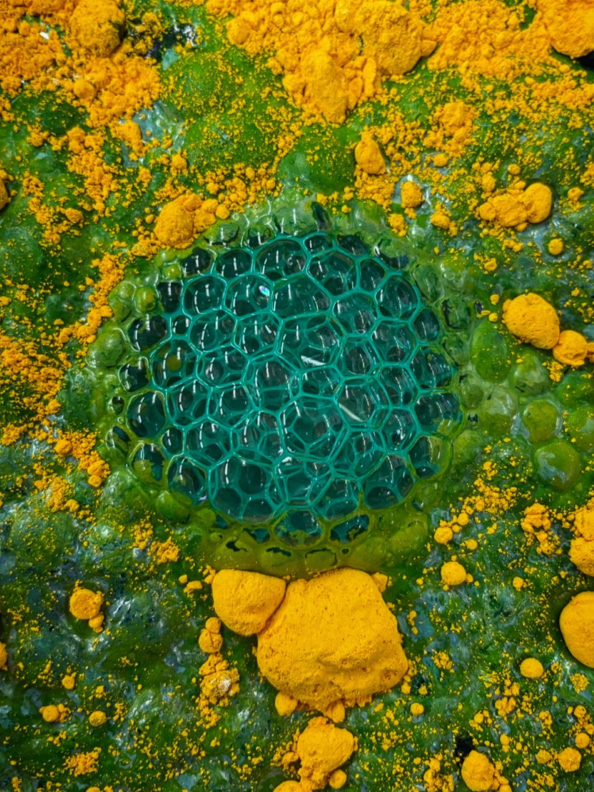 Close-up of a green, honeycomb-like structure surrounded by yellow and green particles.