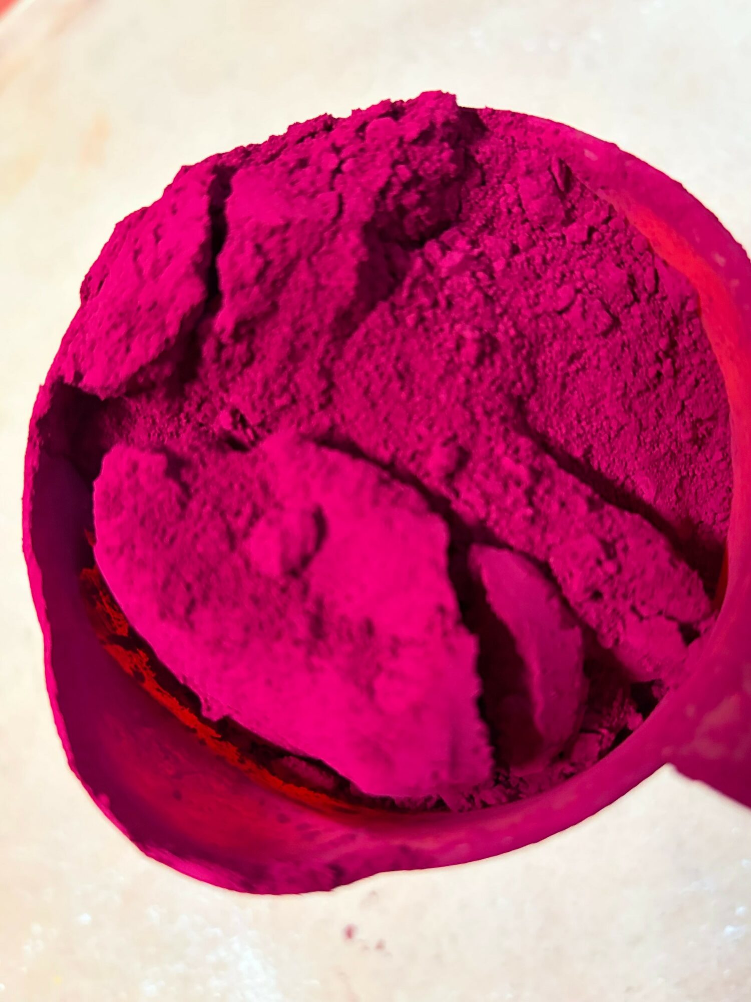 Pink powder in a round container, with a textured surface and a small scoop on the side.