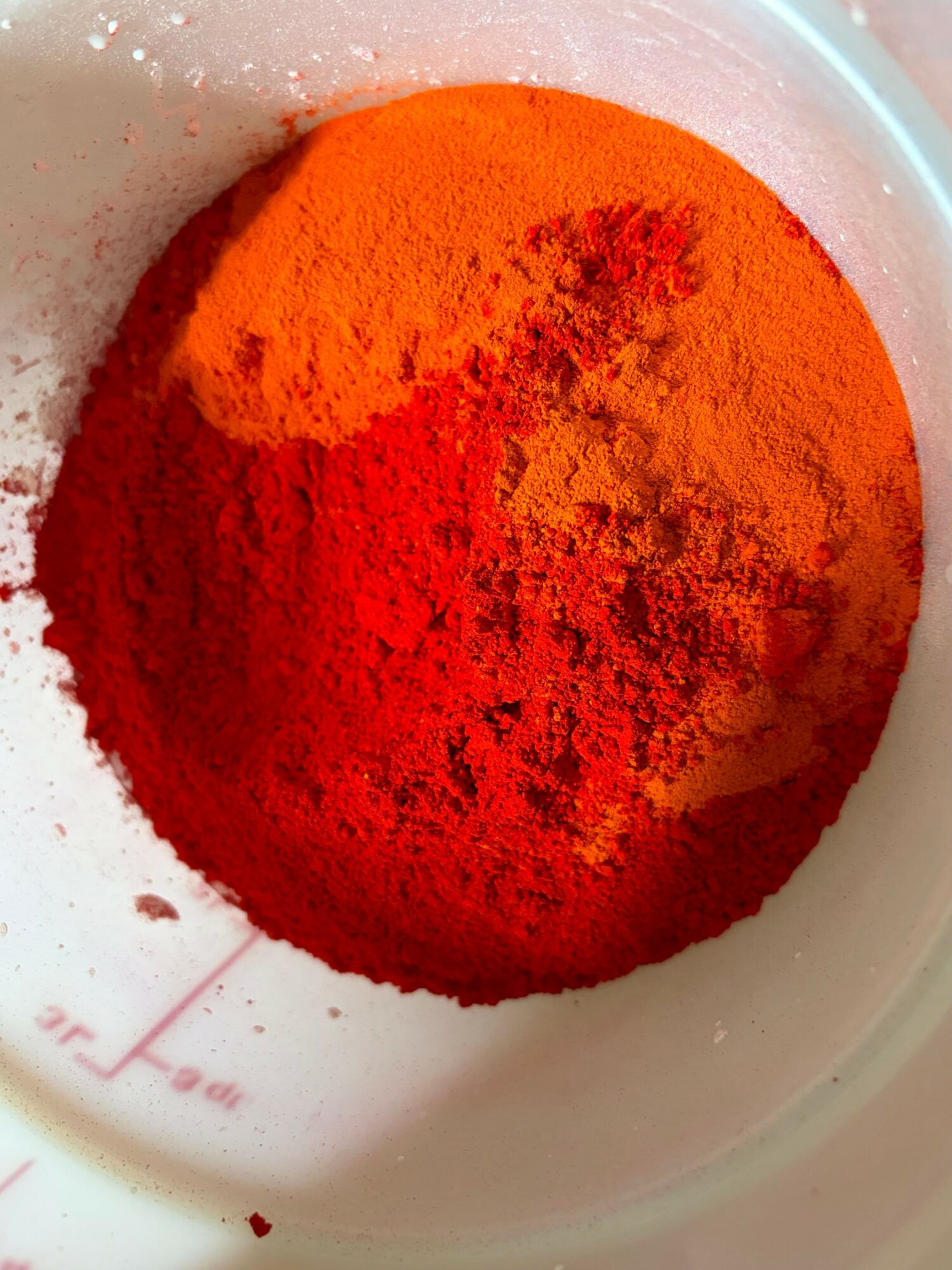 Red and orange powdered spices in a white container, with some powder spilled outside.