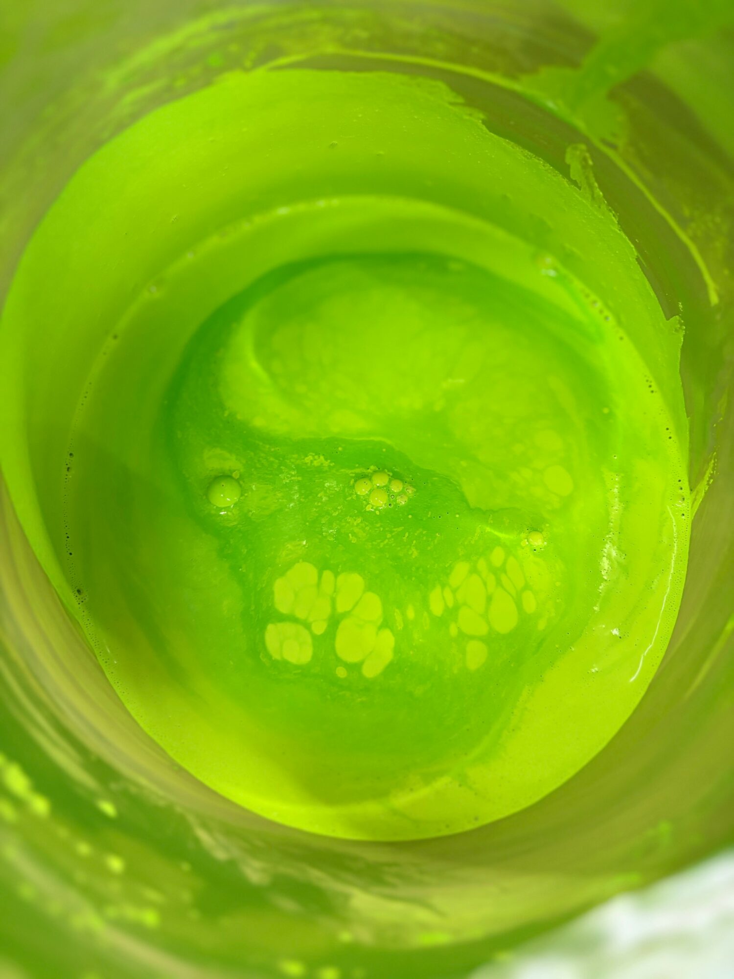 Close-up of a green liquid with bubbles and swirling patterns inside a container.