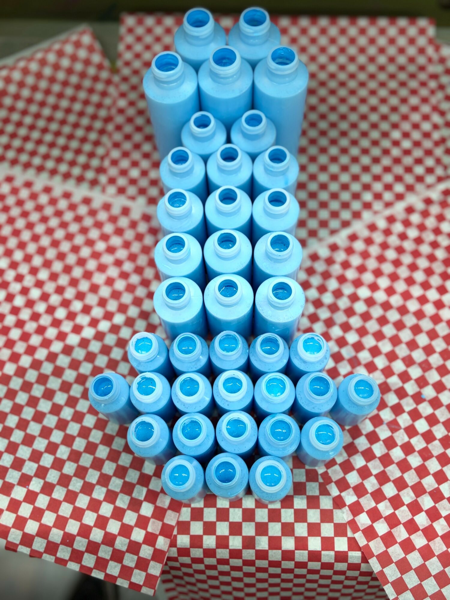 Blue plastic bottles arranged vertically on red and white checkered paper, viewed from the side, with the open ends facing upward.