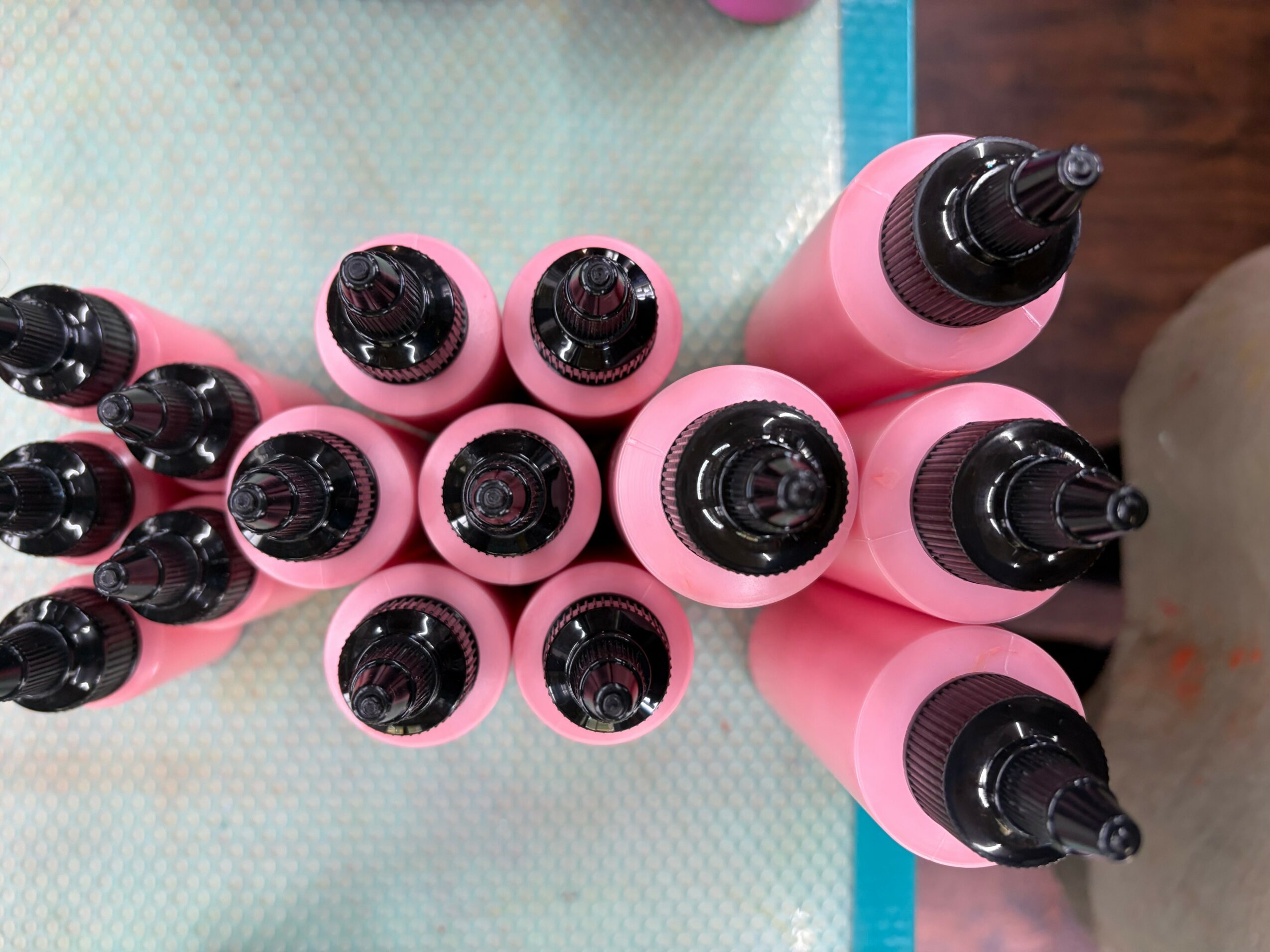Top view of pink bottles with black caps arranged on a surface, some with black dropper caps, some with black spray nozzles.