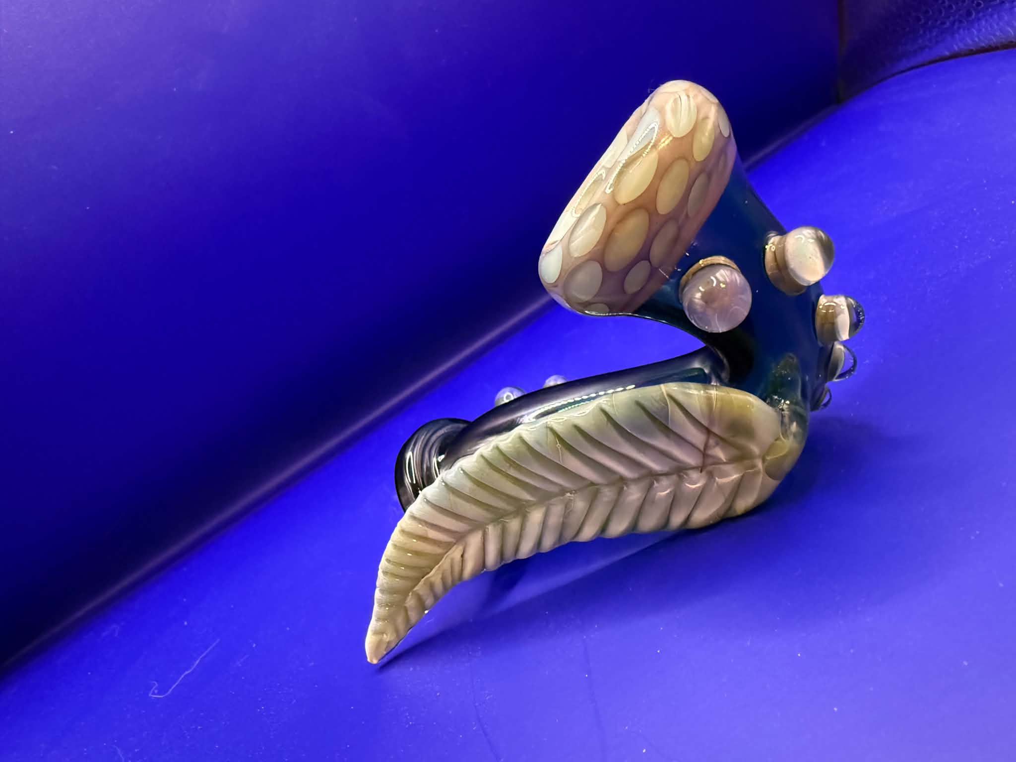Decorative faucet with a leaf-shaped handle and a rounded top, set against a blue background.