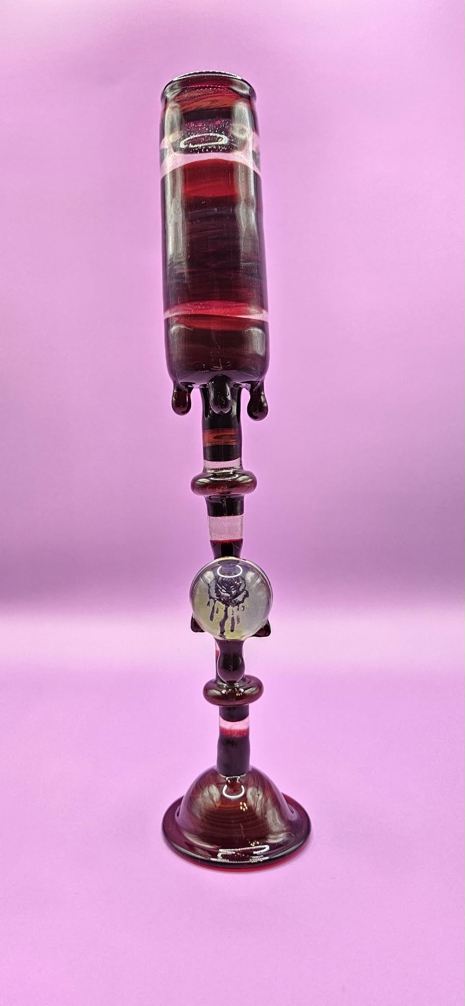 Glass object with a long, vertical shape and intricate design, set against a pink background.