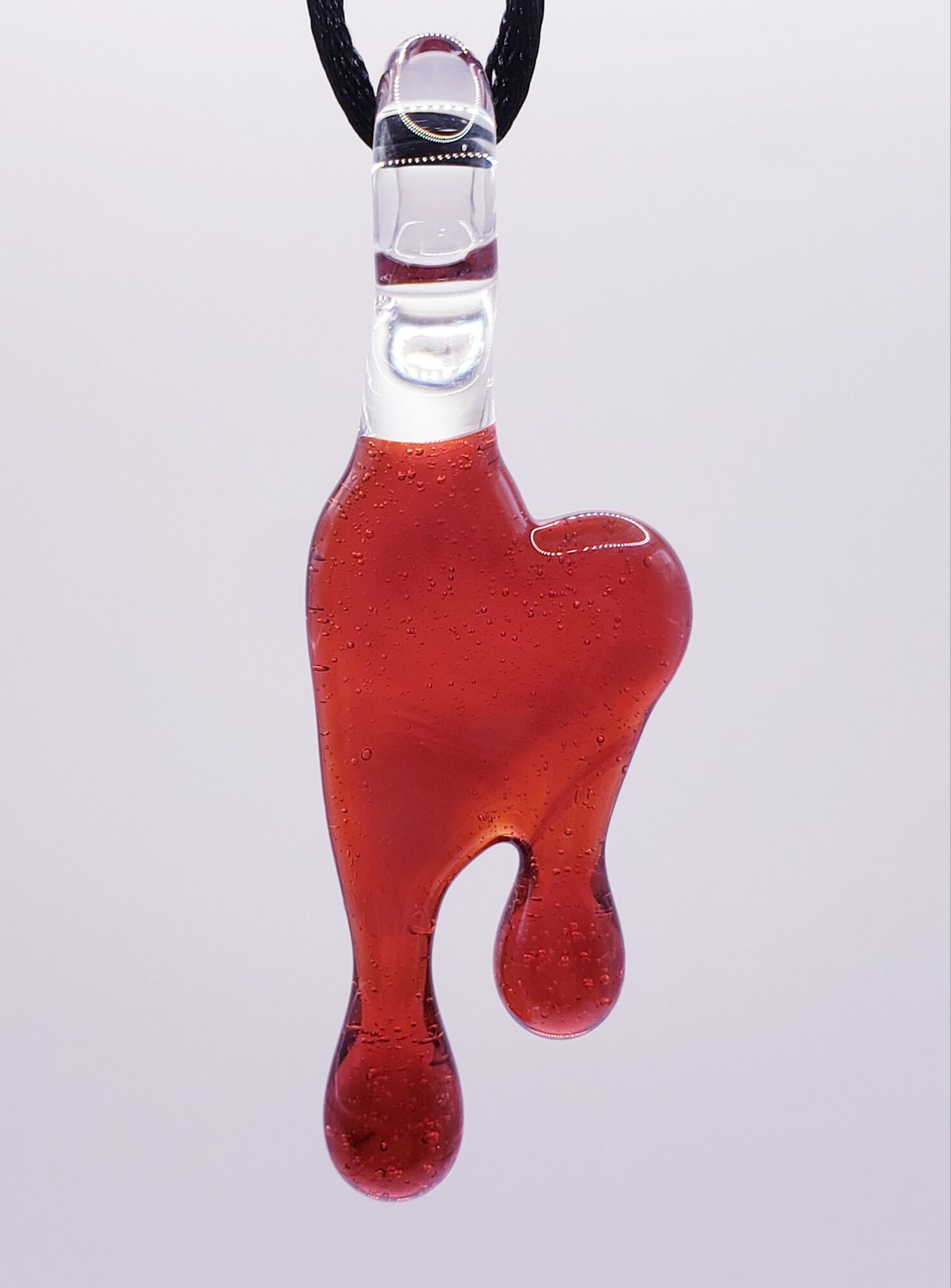 Red glass pendant with an abstract, irregular shape hanging from a black cord.