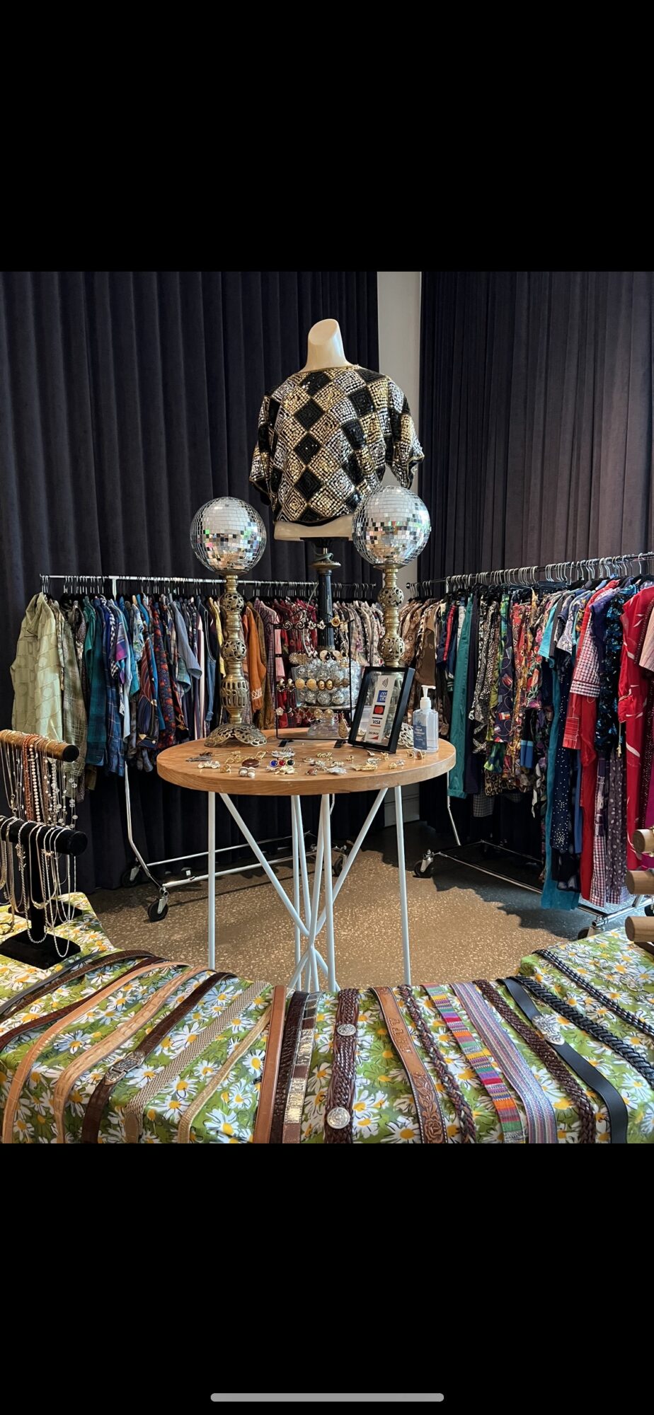 Clothing display with a mannequin wearing a patterned outfit, surrounded by racks of colorful clothes and decorative items.