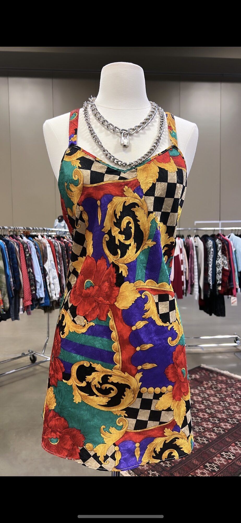 Colorful patterned dress with floral and checkered designs on a mannequin, accessorized with layered necklaces.