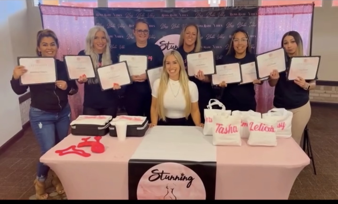 Group of seven people holding certificates, with a table displaying awards and a banner in the background.