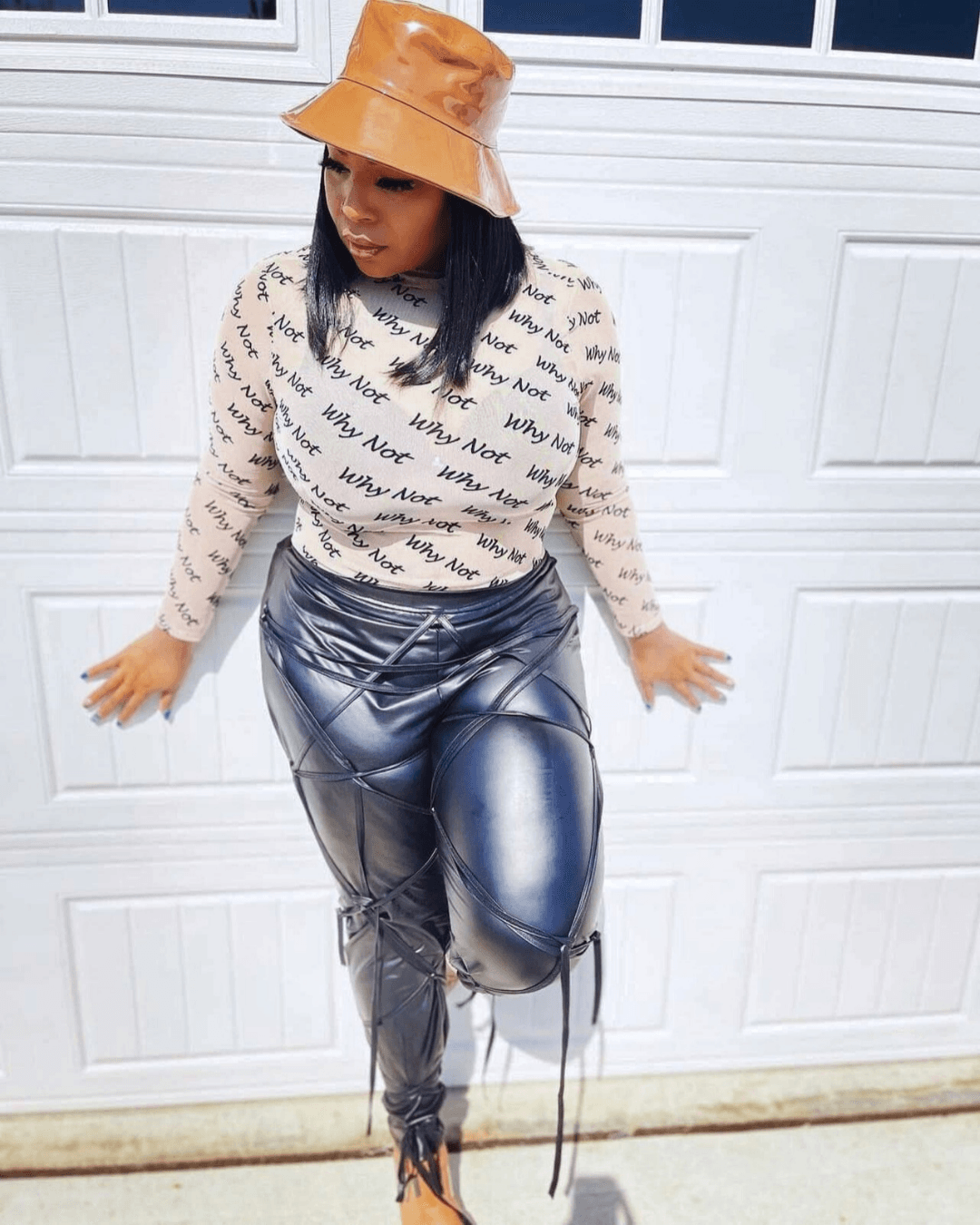 Woman wearing a beige hat, patterned sweater, and shiny metallic pants, standing against a white garage door.