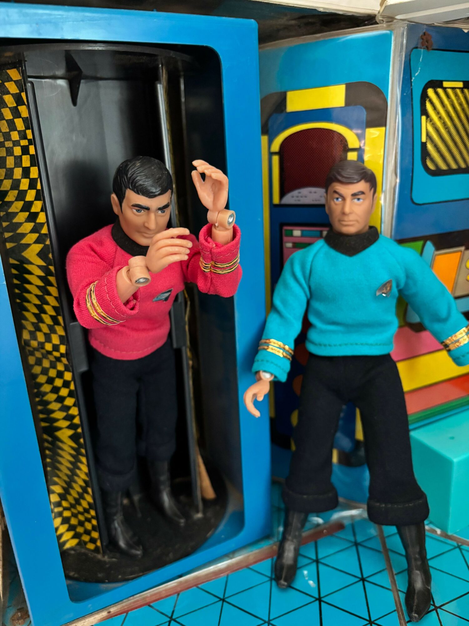 Two people in colorful clothing inside a futuristic-looking room with geometric patterns and vibrant colors.