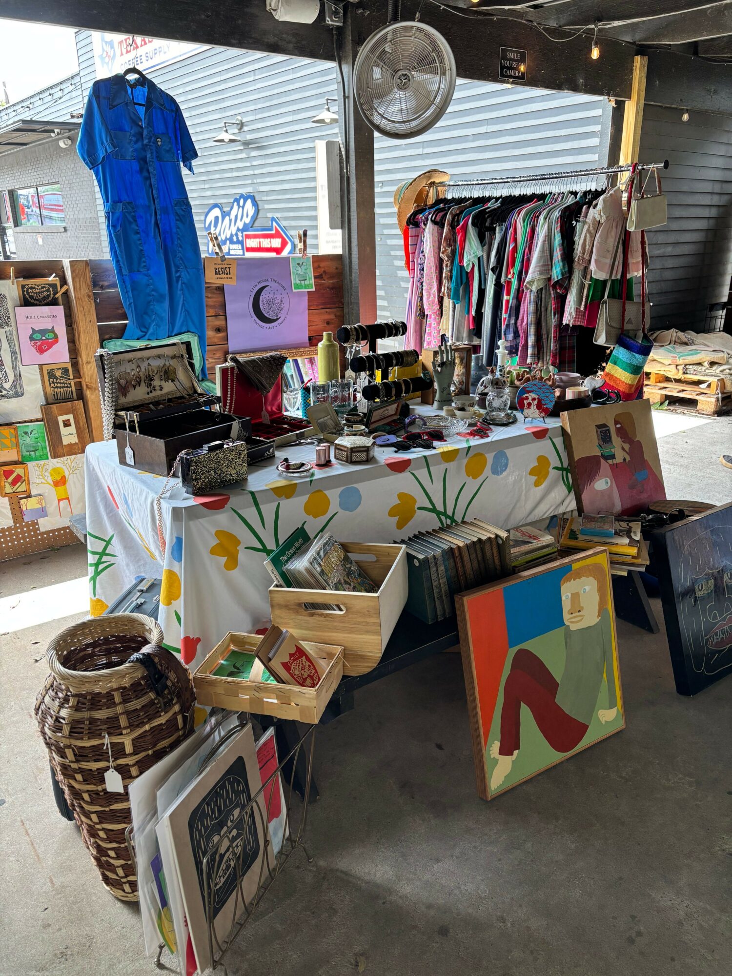 Table with colorful clothing, books, and decorative items in a room with a window and concrete floor.
