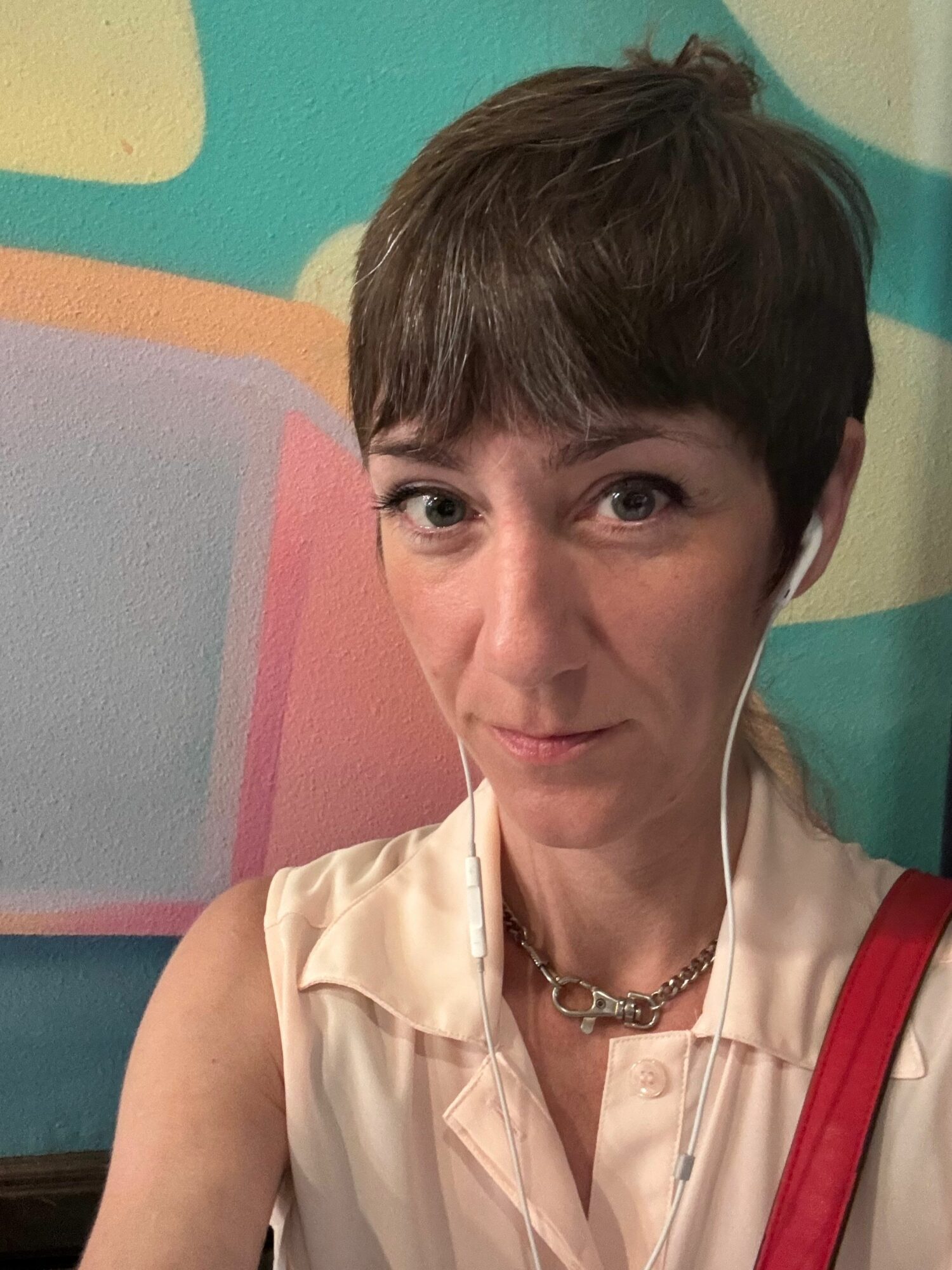 Person with short brown hair wearing a cream-colored shirt with red accents, sitting against a colorful background.