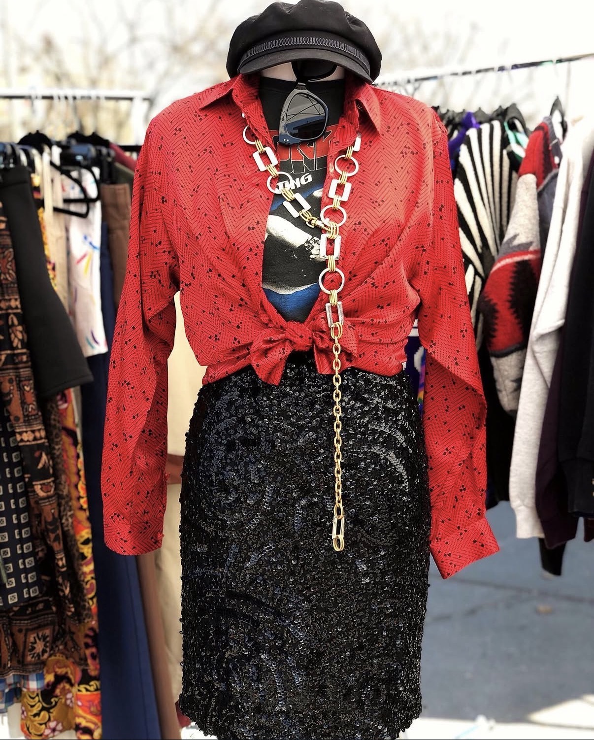 Clothing display with a red shirt, black sequined skirt, and accessories including a chain necklace and hat.