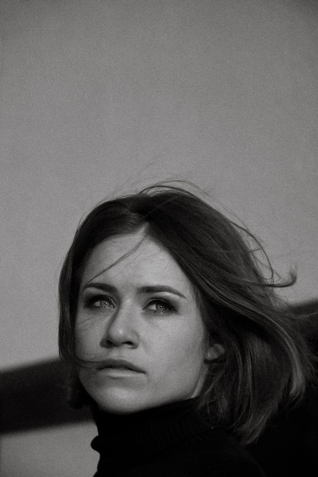 Woman with shoulder-length hair looking to the side, wearing a dark top, against a plain background.