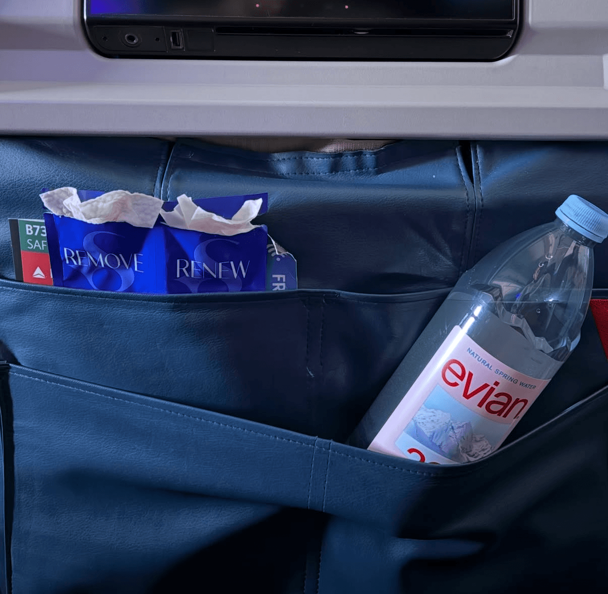 Seat pocket holding tissue packets and a plastic water bottle, with a laptop above. Alt text word count: 24.