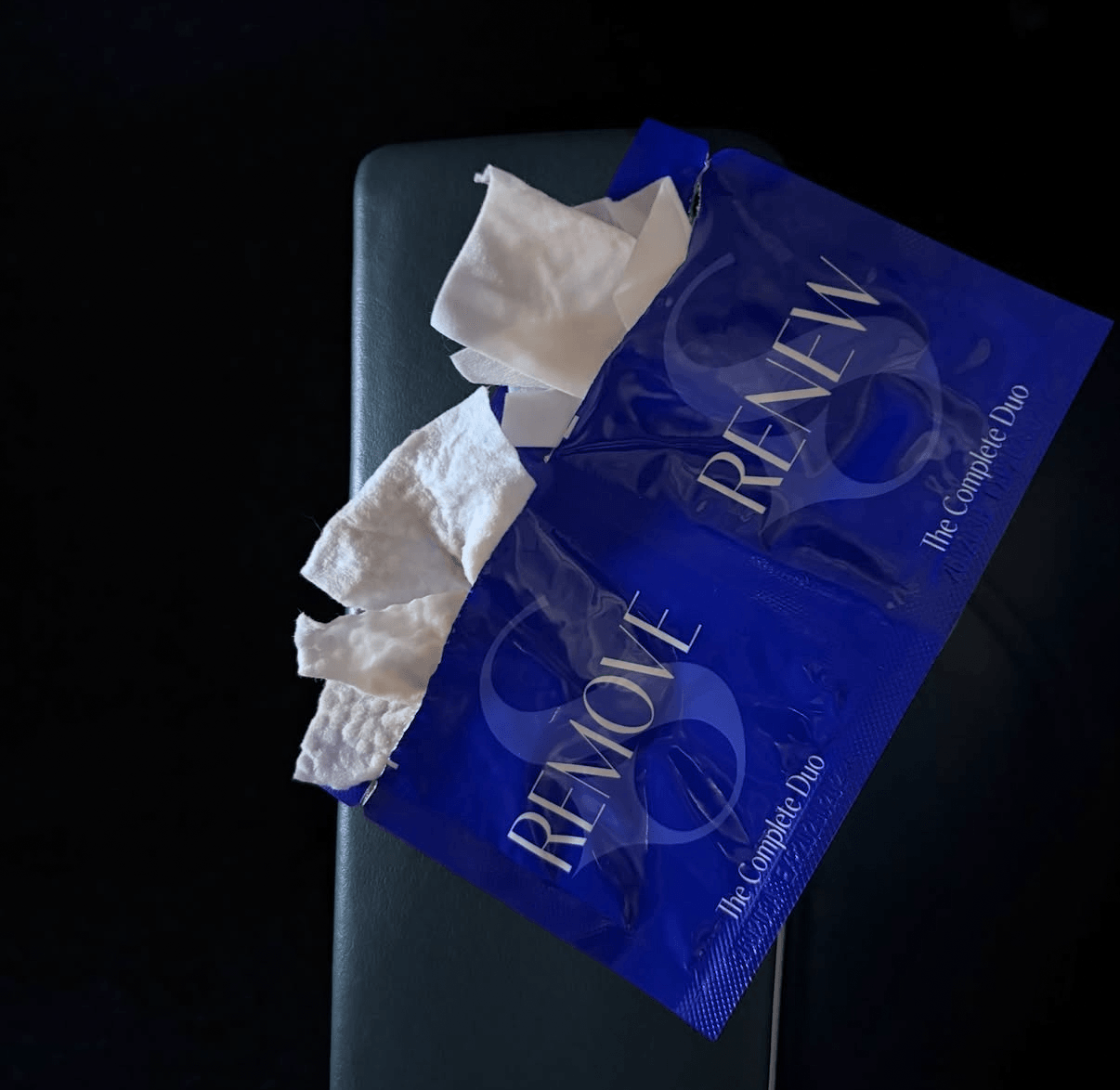 A blue plastic bag with tissues inside, placed on a dark surface.