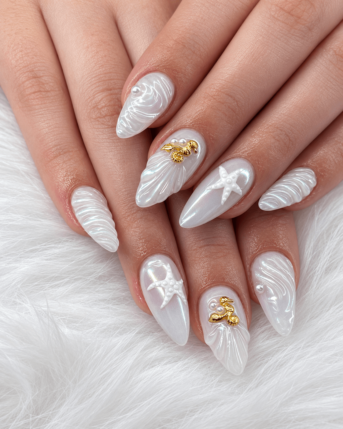 Nail art with white textured designs, starfish and seashell embellishments, and gold accents on long, almond-shaped nails.