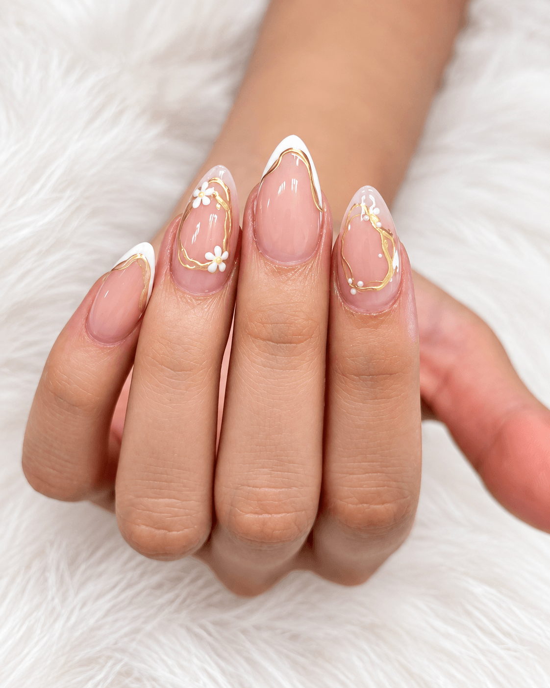 Hand with decorated nails featuring floral and gold accents, resting on a soft white surface.