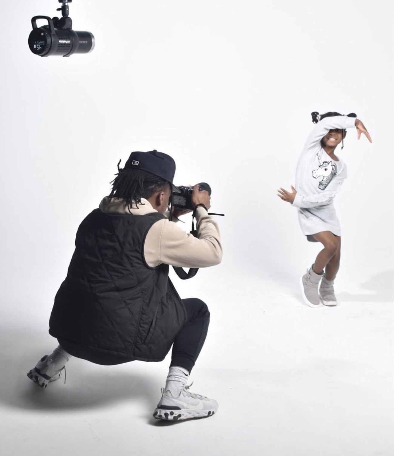 Photographer crouching and taking picture of a girl dancing in a white outfit against a plain white background.
