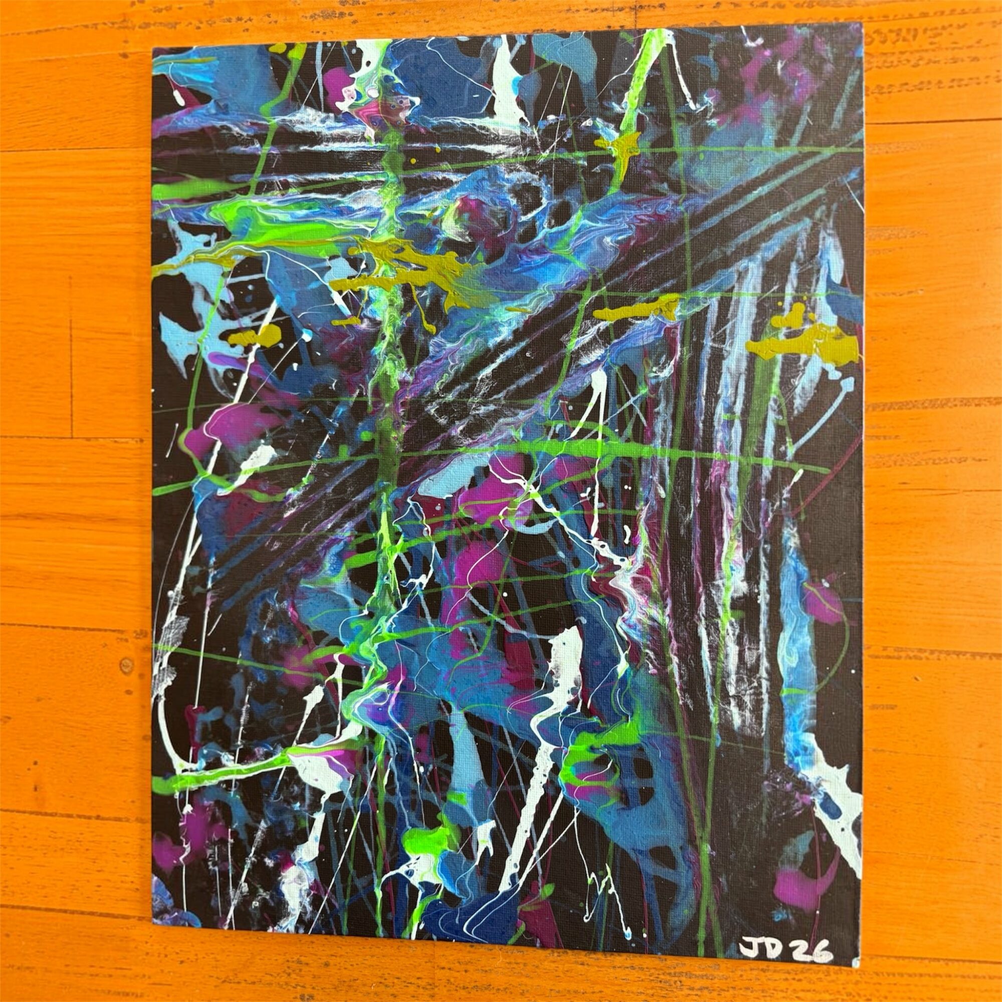 Abstract painting with vibrant splashes of blue, green, purple, and white on a dark background, signed JD 26.